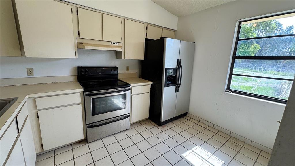 A kitchen features white cabinets, stainless steel appliances, and a tiled floor near a window — 762 KINGS COVE COURT, ORLANDO, FL