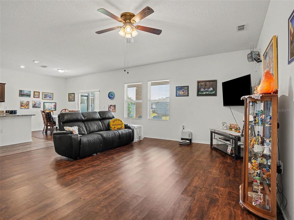 A living room with dark wood-look flooring, a black leather sofa, and a glass display cabinet — 524 BLUE WATER COURT, HAINES CITY, FL