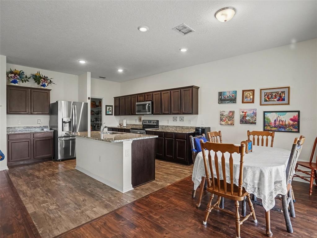 A kitchen with dark wood cabinets, granite countertops, stainless steel appliances, and an adjacent dining area — 524 BLUE WATER COURT, HAINES CITY, FL