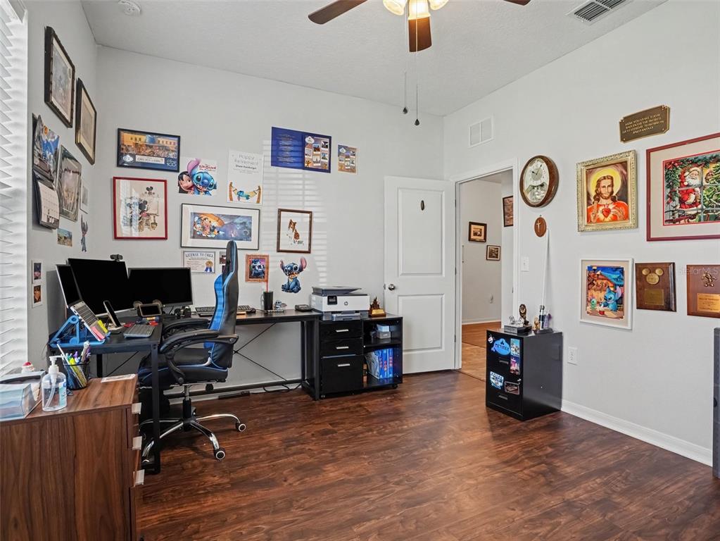 A home office features a desk with dual monitors, wood-look flooring, and walls decorated with art — 524 BLUE WATER COURT, HAINES CITY, FL