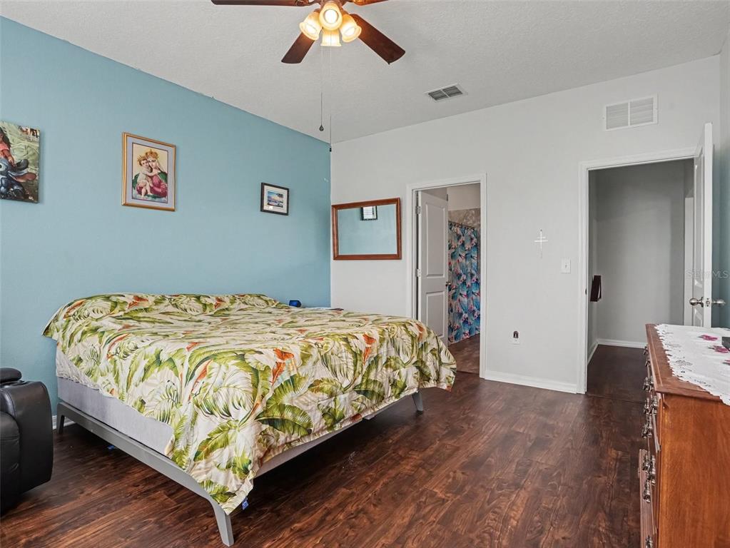 A bedroom features a tropical-print bedspread, a blue accent wall, and dark wood-look flooring — 524 BLUE WATER COURT, HAINES CITY, FL