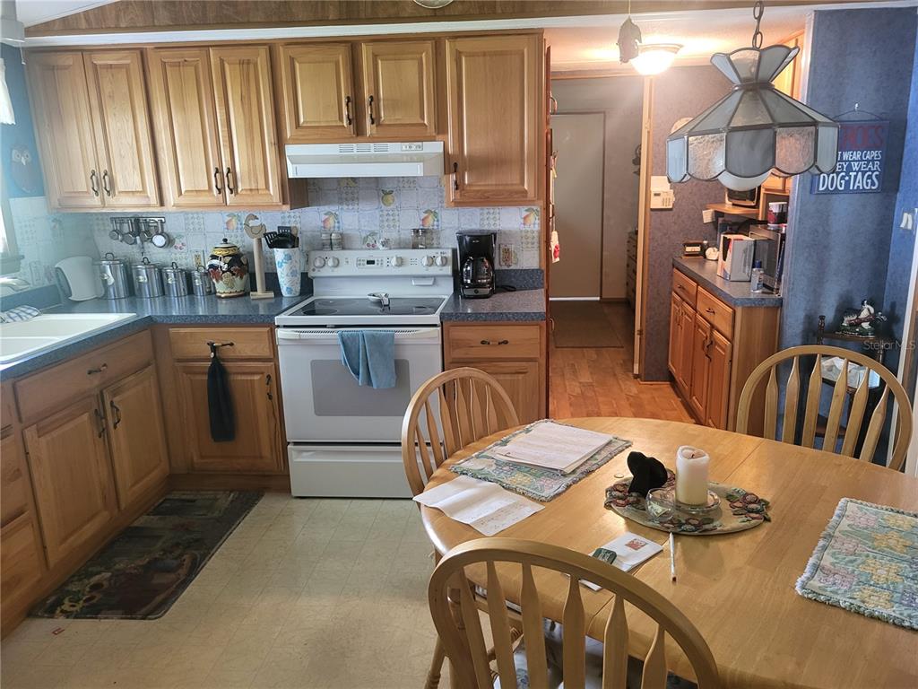 A kitchen features wood cabinets, a white stove, and a round wooden dining table — 2144 LOIS BOULEVARD, LAKE ALFRED, FL