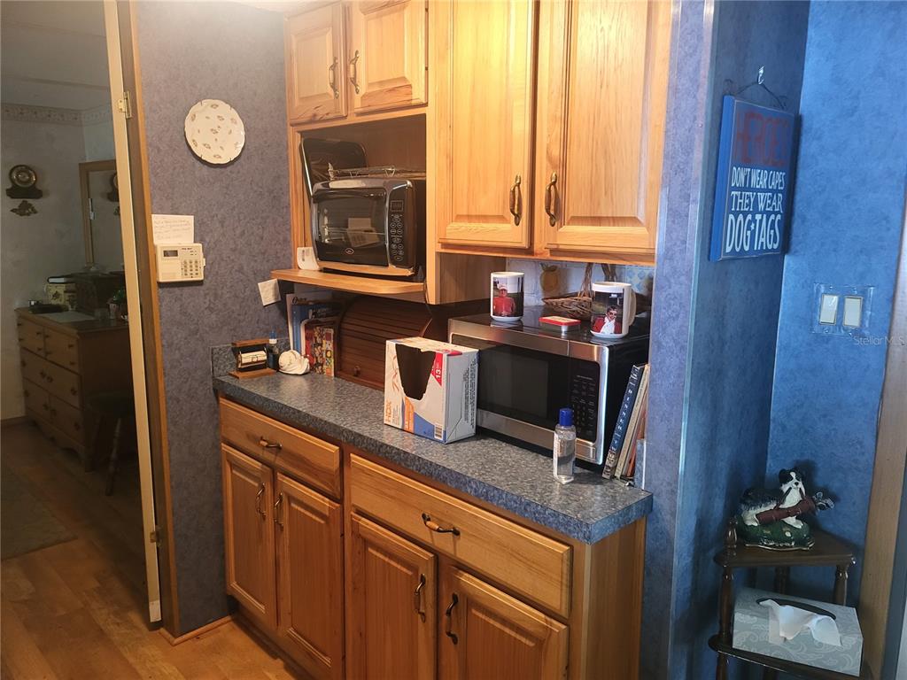 A kitchen area features wood cabinets, blue walls, a countertop with two microwaves, and flooring — 2144 LOIS BOULEVARD, LAKE ALFRED, FL