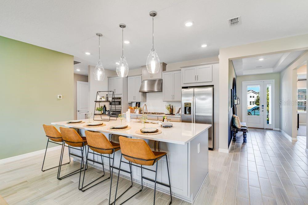 A modern kitchen features a large white island with four leather stools and light cabinetry — 12533 WHARF TERRACE, PALMETTO, FL