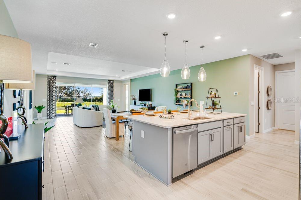 A modern open-concept kitchen with a large island overlooks a living area and dining space — 12533 WHARF TERRACE, PALMETTO, FL