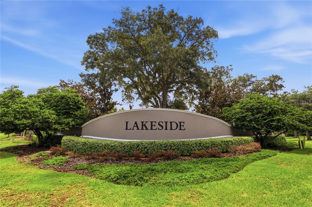 A curved monument sign reading LAKESIDE sits in a landscaped lawn beneath a large tree — 13822 REINDEER CIRCLE, HUDSON, FL