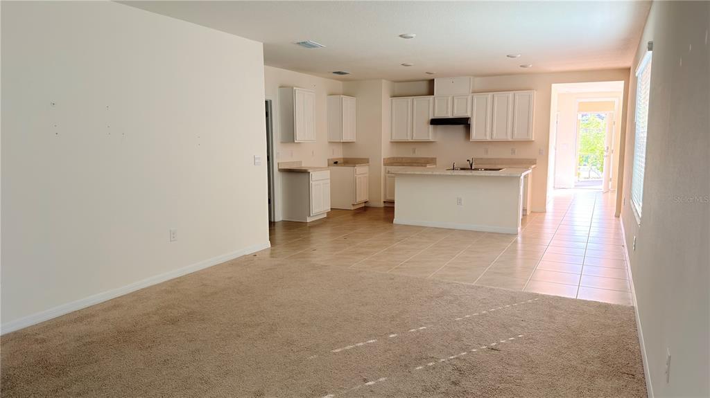 An open-concept living room with beige carpet transitions into a tiled kitchen with white cabinets — 2816 SWOOPING SPARROW DRIVE, ST CLOUD, FL