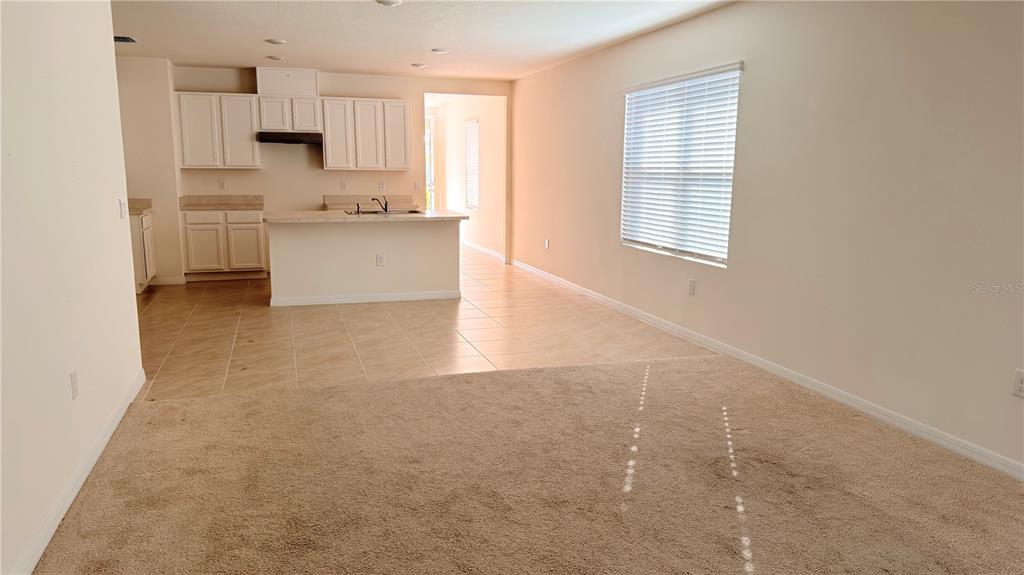A carpeted living area opens to a kitchen with white cabinets and tile flooring — 2816 SWOOPING SPARROW DRIVE, ST CLOUD, FL