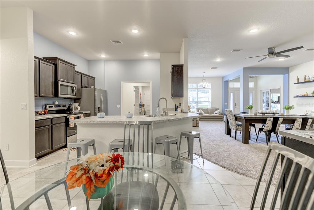 A kitchen with dark cabinets and a breakfast bar overlooks a dining and living area — 71 BELLS OF IRELAND COURT, HOMOSASSA, FL
