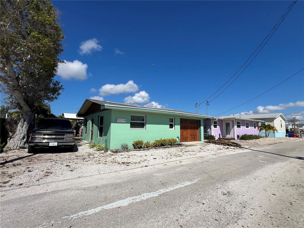 A light green single-story house with a garage and a gravel driveway sits outdoors — 2650 COCO PLUM DRIVE, MATLACHA, FL