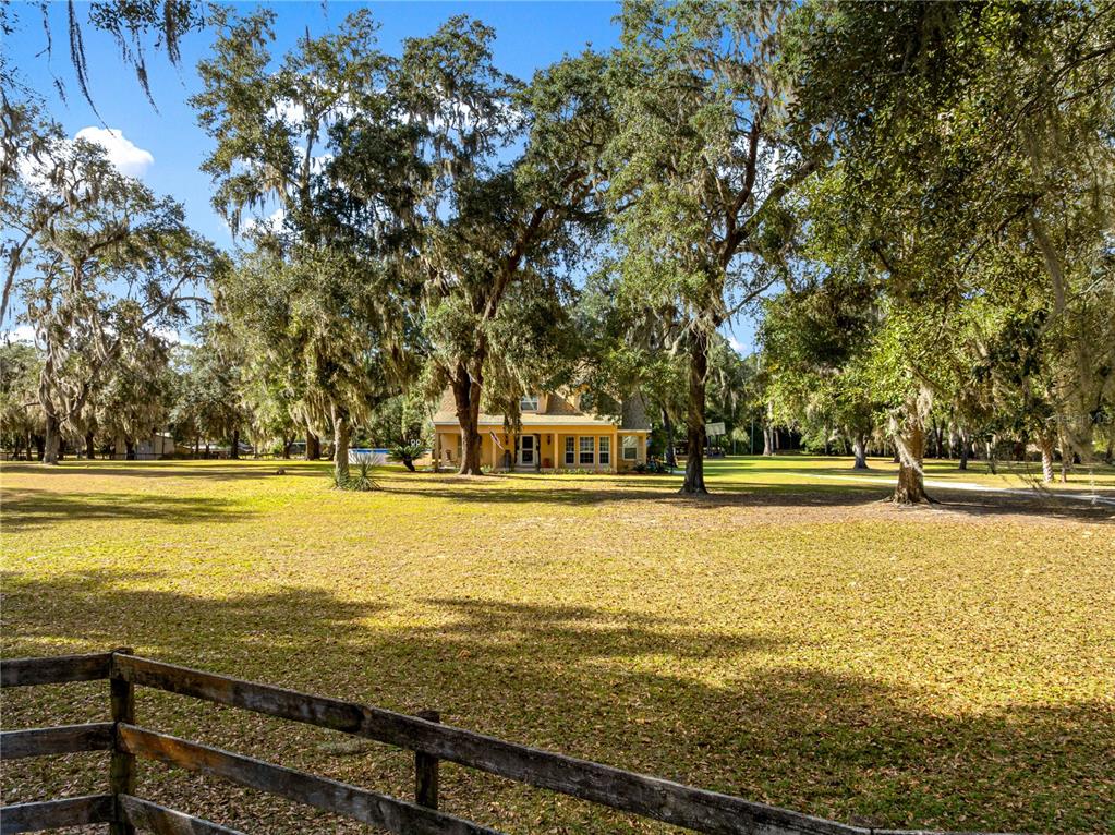 A yellow house sits in a large, tree-filled yard behind a wooden fence — 13850 NE 47TH AVENUE, ANTHONY, FL