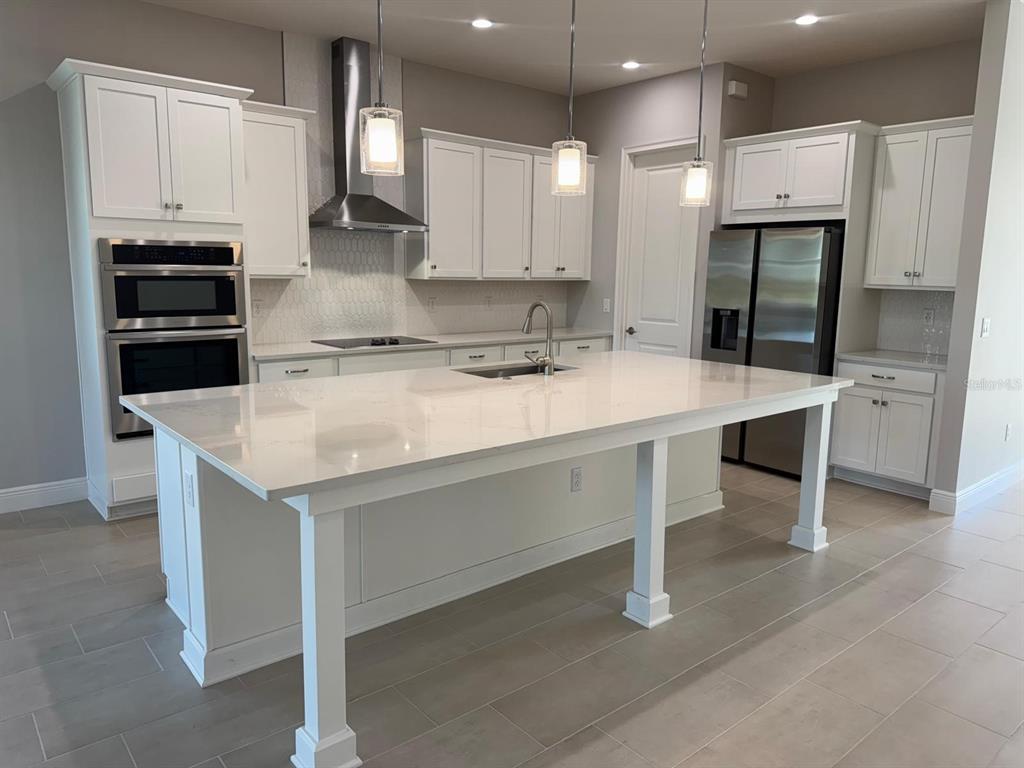 A modern kitchen features white cabinetry, a large quartz island, and stainless steel appliances — 1134 CLIFFHAVEN COURT, ORMOND BEACH, FL