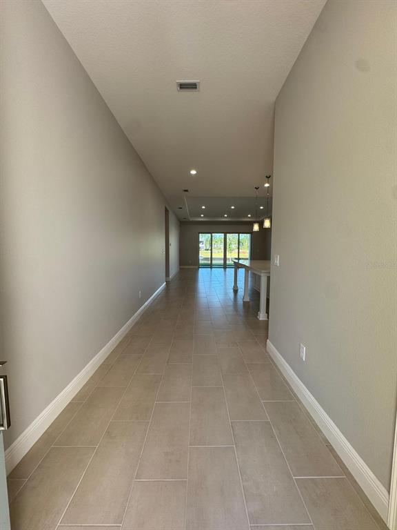 A long hallway with light tile flooring leads toward an open kitchen and glass sliding doors — 1134 CLIFFHAVEN COURT, ORMOND BEACH, FL