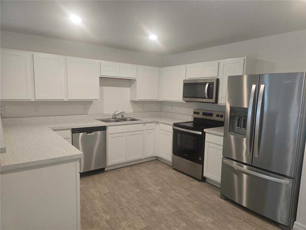 A kitchen features white cabinets, stainless steel appliances, and light-colored countertops — 53 ORCHID COURT, POINCIANA, FL