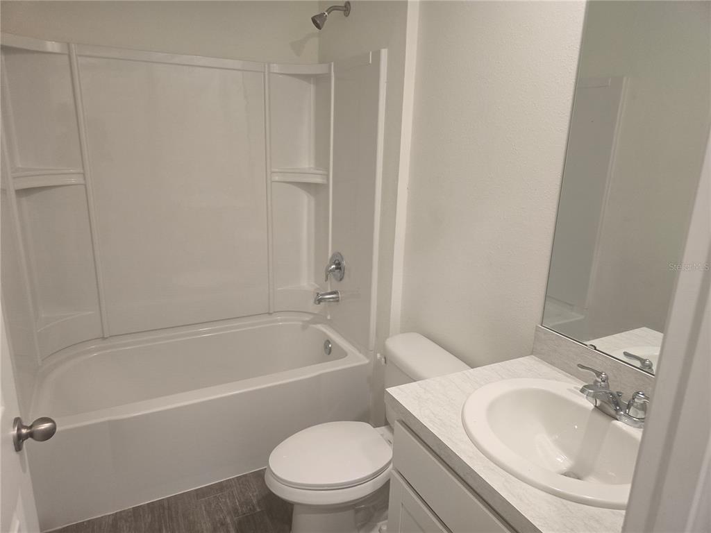 A bathroom features a white tub-shower combination, a toilet, and a vanity with a sink — 53 ORCHID COURT, POINCIANA, FL