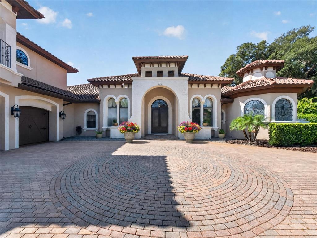 The exterior of a Mediterranean-style home features a circular paver driveway and arched entryways — 7765 ISLEWOOD COURT, SANFORD, FL