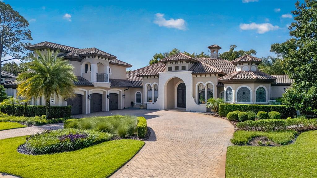A large Mediterranean-style house with a tile roof, arched entryway, and a paved circular driveway — 7765 ISLEWOOD COURT, SANFORD, FL