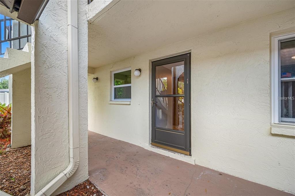 A covered concrete walkway leads to a brown storm door on a beige stucco building — 1100 E BAY DRIVE UNIT 82, LARGO, FL