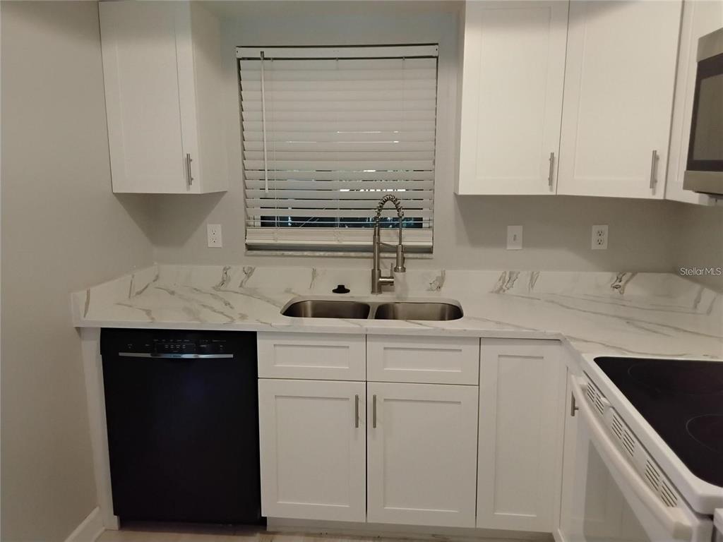 A kitchen features white cabinets, marble-look countertops, a stainless steel sink, and a dishwasher — 1100 E BAY DRIVE UNIT 82, LARGO, FL