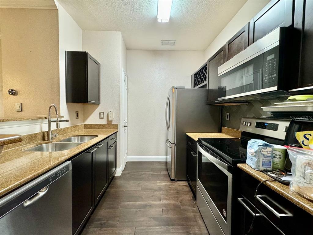 A galley kitchen features dark cabinets, granite countertops, stainless steel appliances, and wood-look flooring — 5000 CULBREATH KEY WAY UNIT 1-318, TAMPA, FL