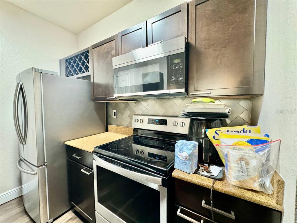 A kitchen features dark wood cabinets, stainless steel appliances, and a herringbone-patterned tile backsplash — 5000 CULBREATH KEY WAY UNIT 1-318, TAMPA, FL