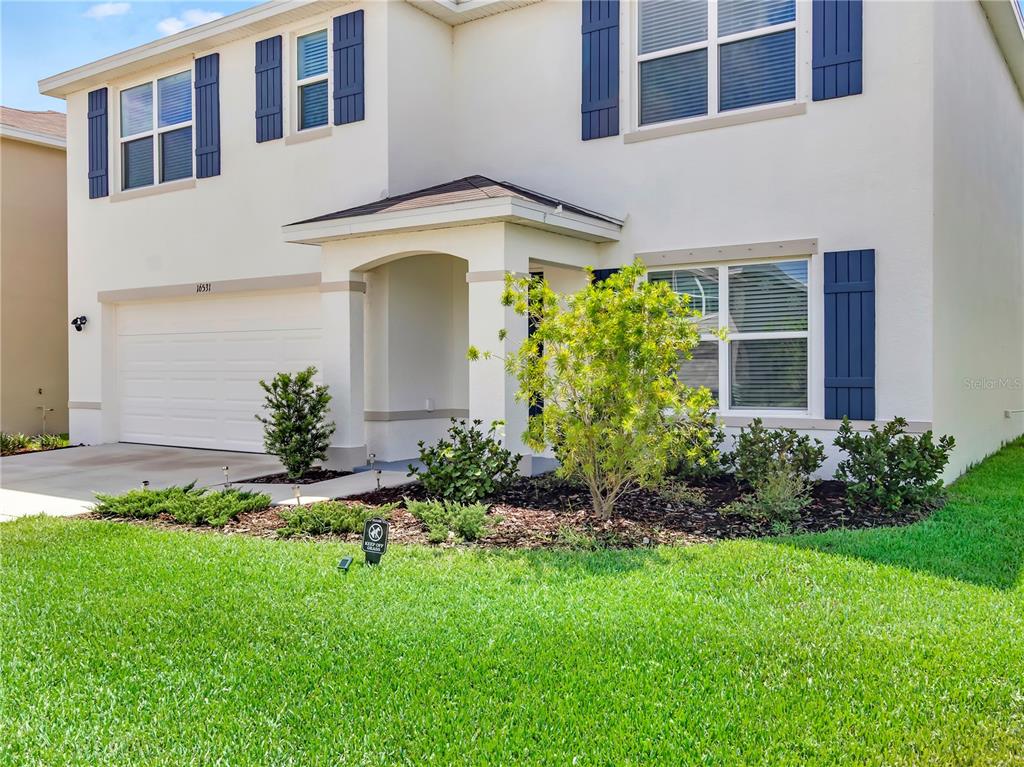 A two-story house with white stucco siding, blue shutters, a garage, and front landscaping — 16531 WINDMILL FORGE PASS, WIMAUMA, FL