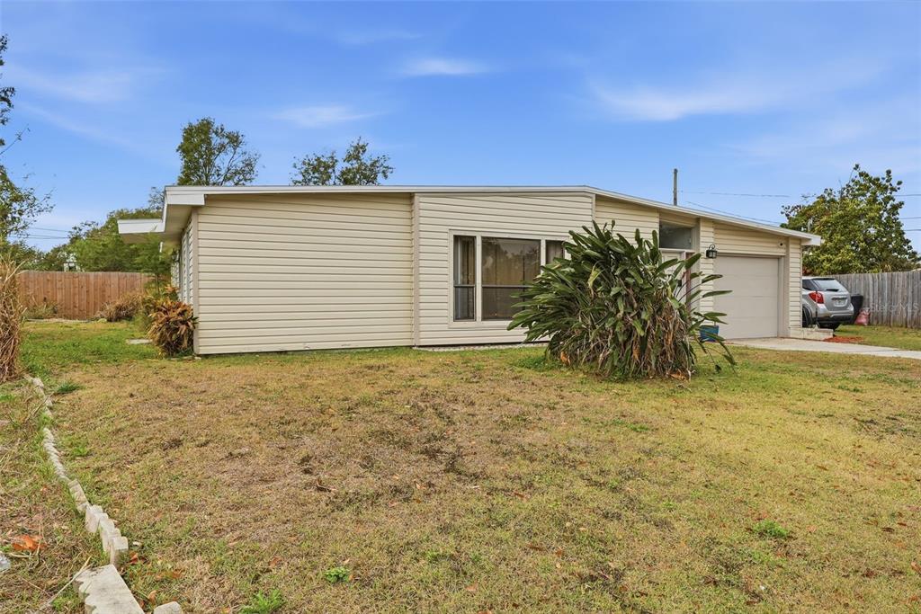 A single-story house with beige siding, a garage, and a large plant in the yard — 1709 CARNEGIE CIRCLE, TAMPA, FL