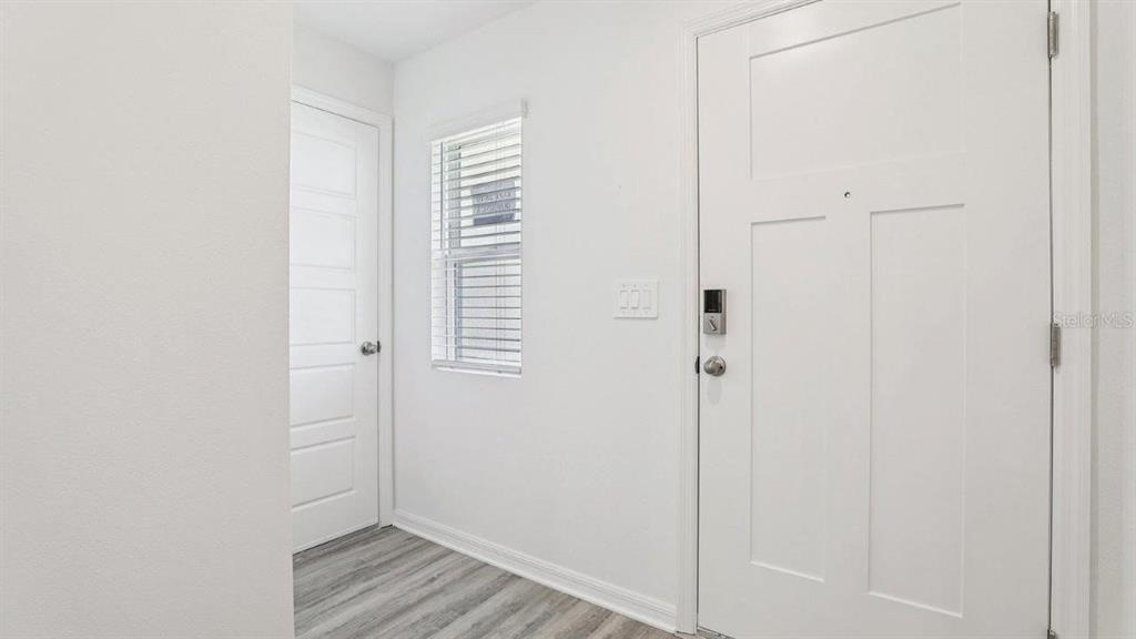 A bright entryway features a white front door, a side door, a window, and wood-look flooring — 5580 TAVERNA LOOP, WINTER HAVEN, FL