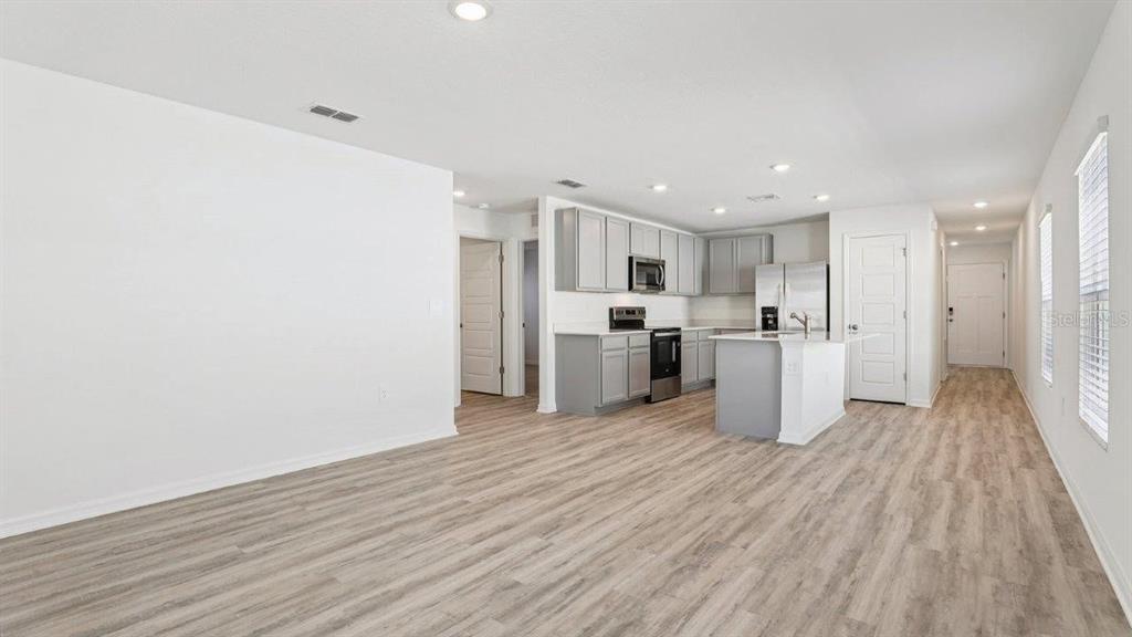 An open-concept kitchen and living area features light wood-look flooring and gray cabinetry — 5580 TAVERNA LOOP, WINTER HAVEN, FL