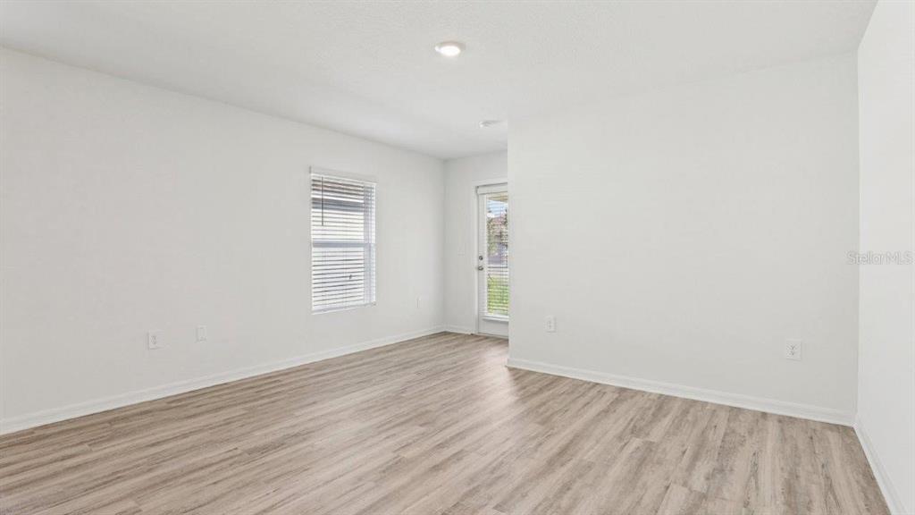 An empty room features white walls, light wood-look flooring, a window, and a glass door — 5580 TAVERNA LOOP, WINTER HAVEN, FL