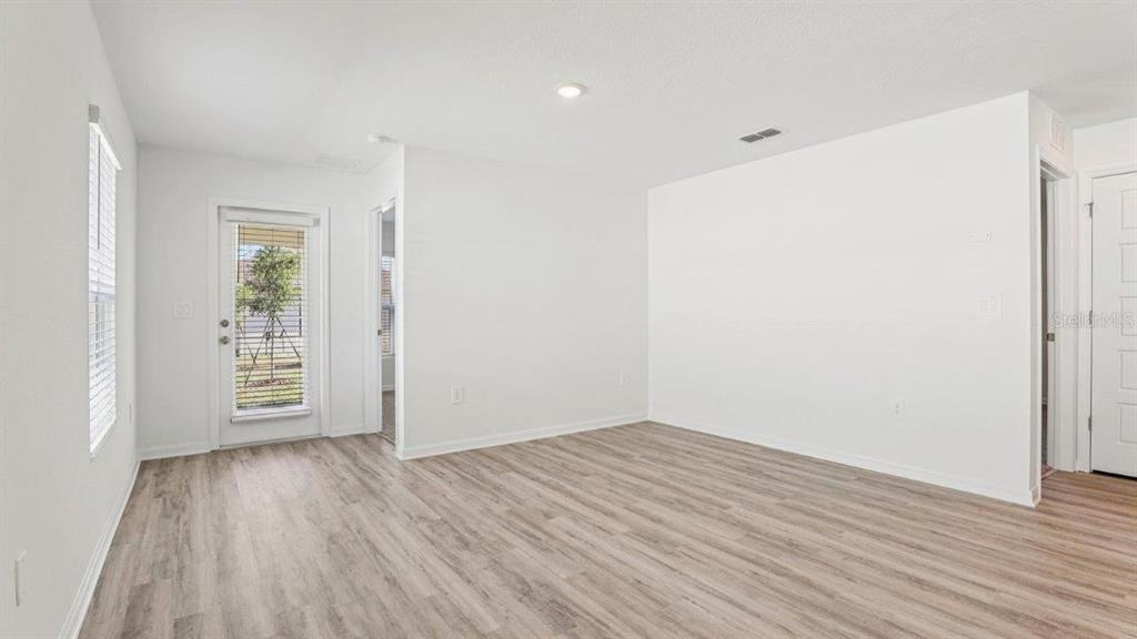 An empty room with light wood-look flooring, white walls, a glass door, and recessed lighting — 5580 TAVERNA LOOP, WINTER HAVEN, FL