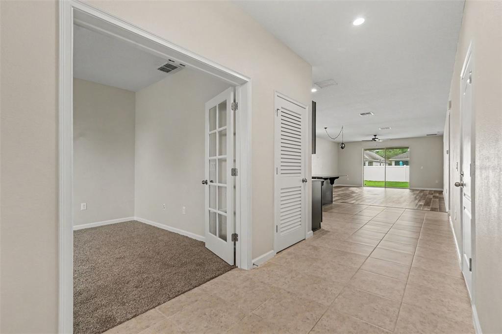 A hallway with tile flooring leads to a carpeted room with French doors and a kitchen — 12318 EAGLE SWOOP PLACE, RIVERVIEW, FL