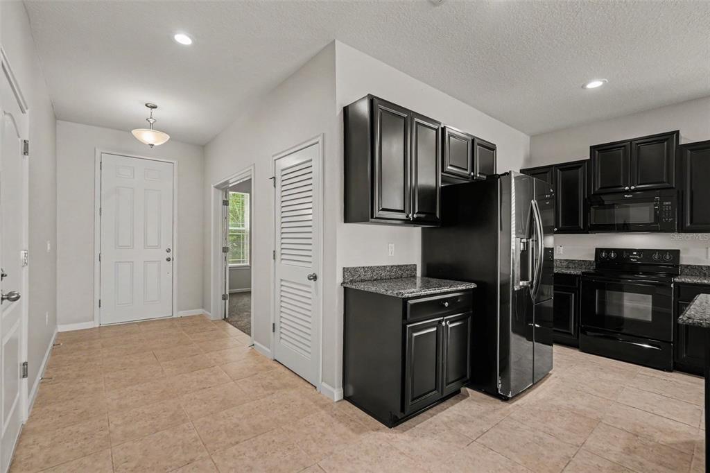 A kitchen features black cabinets, granite countertops, stainless steel appliances, and light-colored tile flooring — 12318 EAGLE SWOOP PLACE, RIVERVIEW, FL