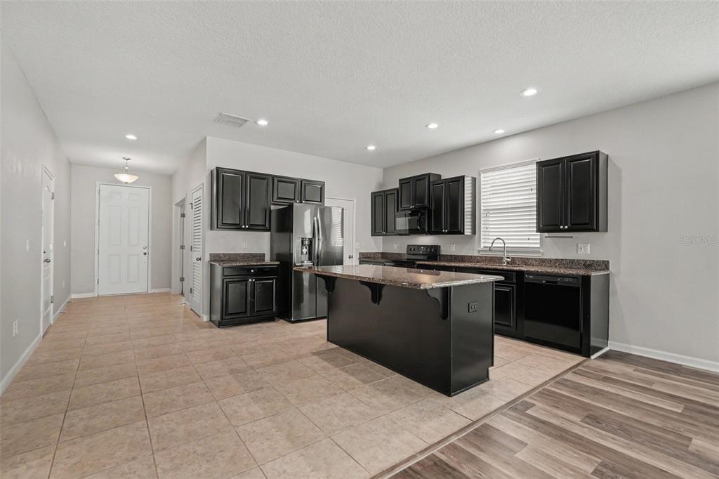 A kitchen features dark cabinetry, a granite-topped island, stainless steel appliances, and tile flooring — 12318 EAGLE SWOOP PLACE, RIVERVIEW, FL