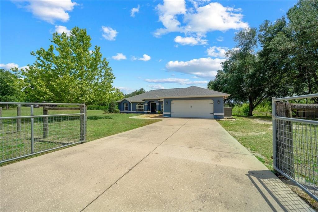 A single-story house with a garage sits behind a fenced yard and concrete driveway — 11985 SE 123RD AVENUE, OCKLAWAHA, FL