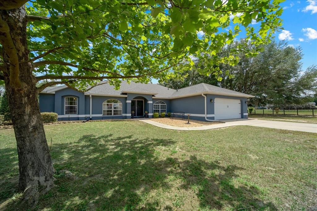 A single-story house with a two-car garage sits behind an open metal gate — 11985 SE 123RD AVENUE, OCKLAWAHA, FL