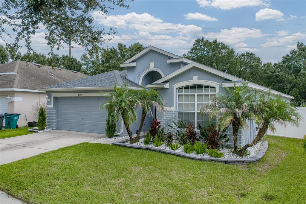 A single-story blue house with a two-car garage, arched entryway, and landscaped front yard — 34455 CLIFFCREEK COURT, WESLEY CHAPEL, FL