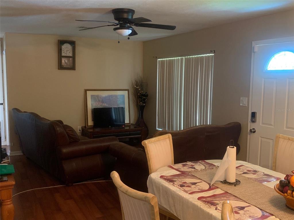 A living room with dark leather sofas, a ceiling fan, and an adjacent dining area — 1406 PEMBROOK DRIVE, LEESBURG, FL