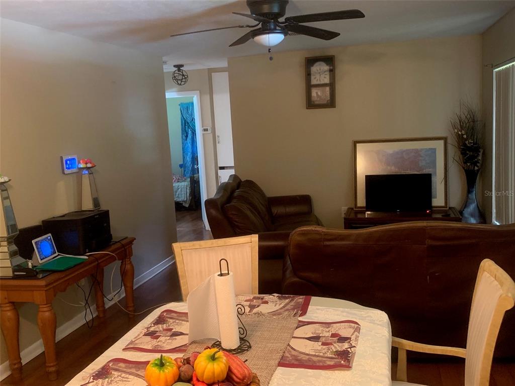 A dining area in the foreground leads into a living room with brown leather sofas — 1406 PEMBROOK DRIVE, LEESBURG, FL