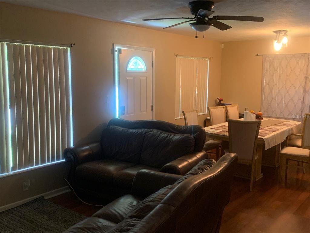 A living room and dining area feature dark leather sofas, wood flooring, and vertical blinds — 1406 PEMBROOK DRIVE, LEESBURG, FL