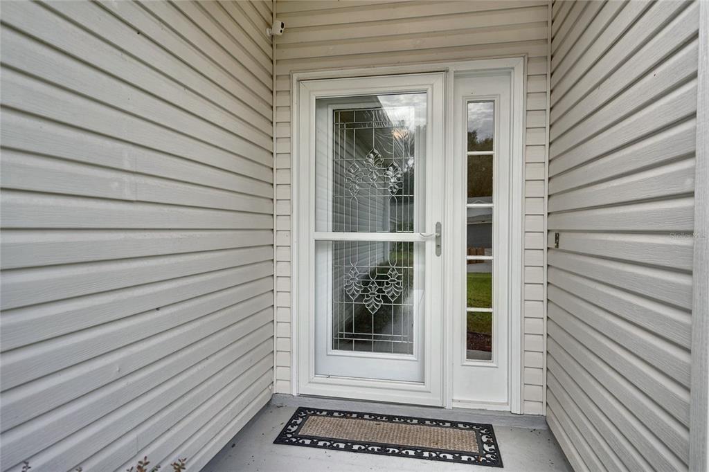 A white storm door with decorative glass panels is set in a light-colored vinyl-sided entryway — 25735 GLEN EAGLE DRIVE, LEESBURG, FL