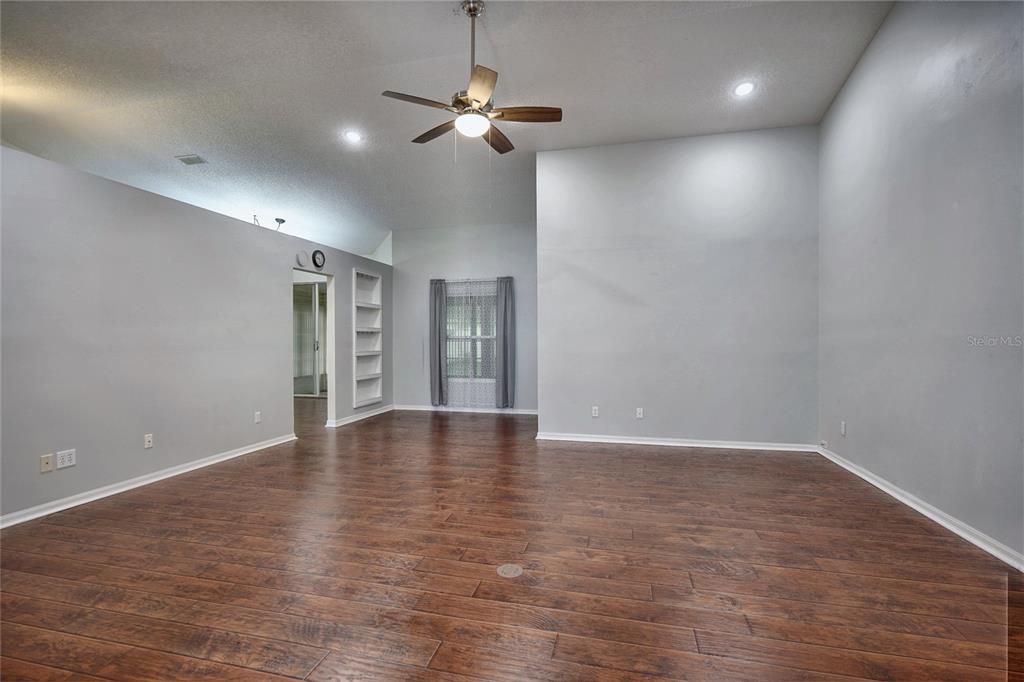 An empty living room features wood-look flooring, light gray walls, a ceiling fan, and built-in shelving — 25735 GLEN EAGLE DRIVE, LEESBURG, FL