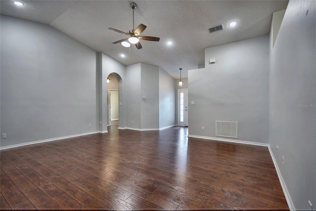 An empty room with gray walls, dark wood-look flooring, a ceiling fan, and an arched doorway — 25735 GLEN EAGLE DRIVE, LEESBURG, FL