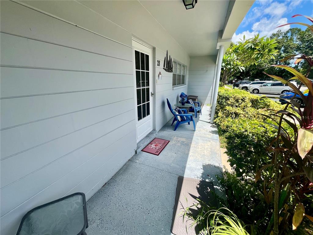 A covered porch features a white door, blue chairs, and a welcome mat — 2460 FRANCISCAN DRIVE UNIT 28, CLEARWATER, FL