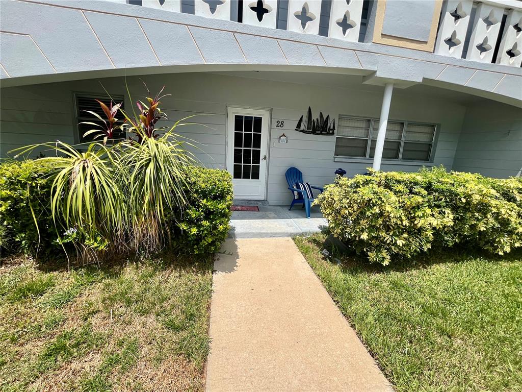 A concrete walkway leads to the front entrance of a residential unit with a blue chair — 2460 FRANCISCAN DRIVE UNIT 28, CLEARWATER, FL