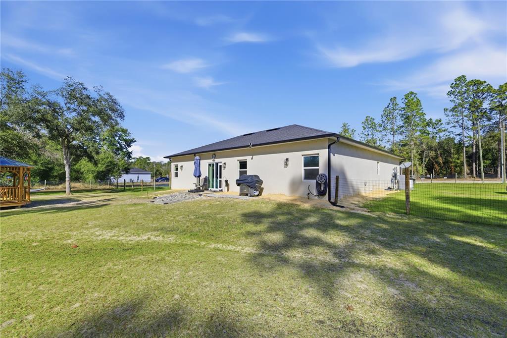 The exterior rear view of a single-story house features a patio, grill, and fenced yard — 13920 NE 6TH STREET, WILLISTON, FL