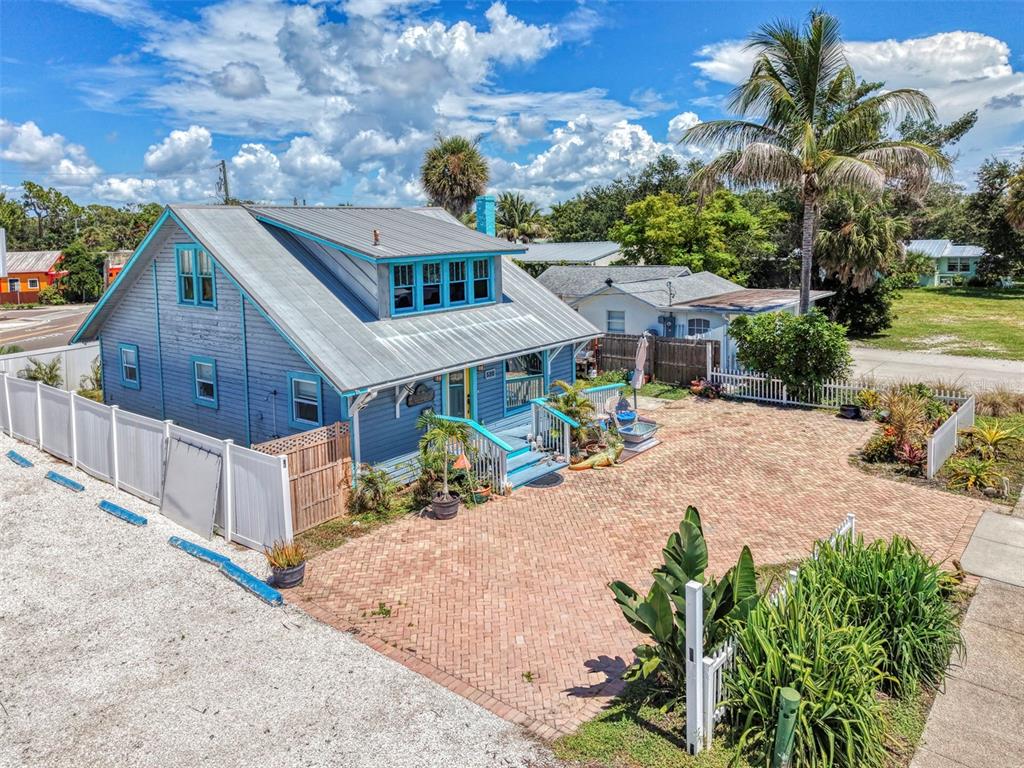 A blue house with a metal roof and brick driveway sits behind a white fence — 530 W GREEN STREET, ENGLEWOOD, FL