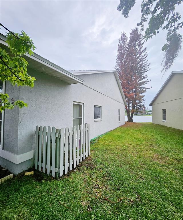 The side exterior of a house features a small white fence enclosing an HVAC unit — 14601 POTANOW TRAIL, ORLANDO, FL