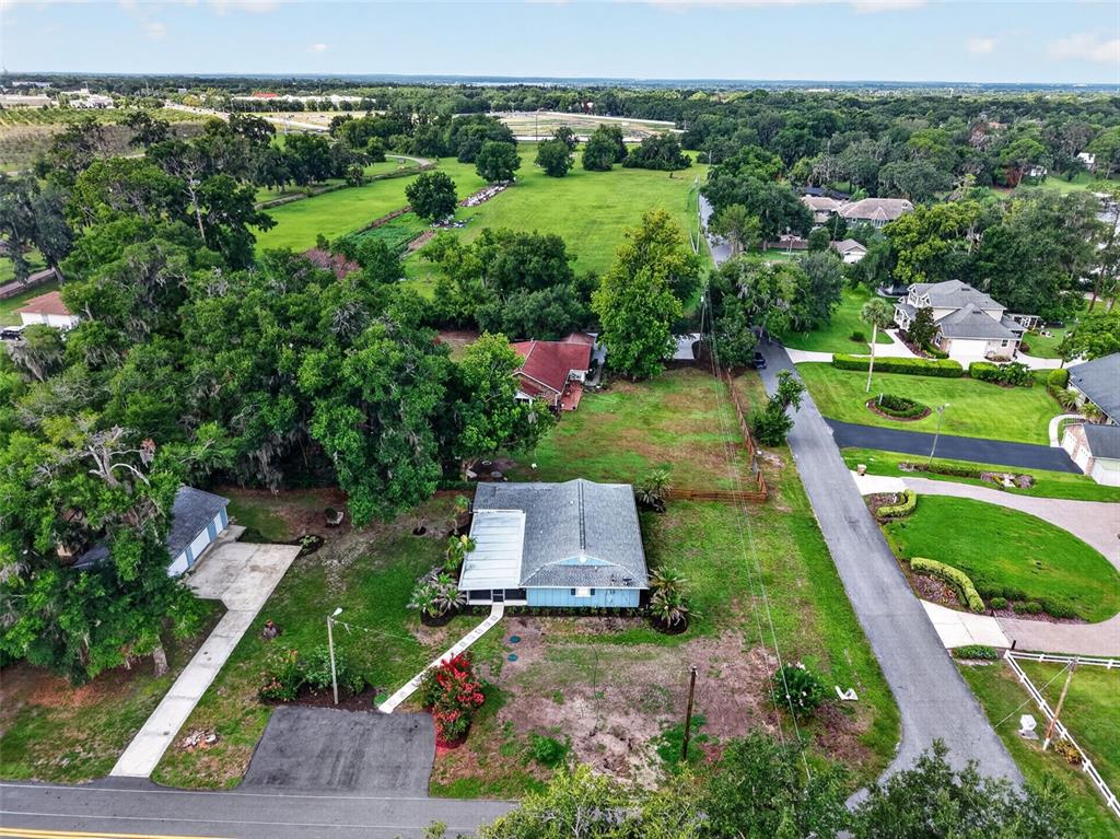 An aerial view shows a blue house with a gray roof surrounded by green lawns — 33350 E LAKE JOANNA DRIVE, EUSTIS, FL