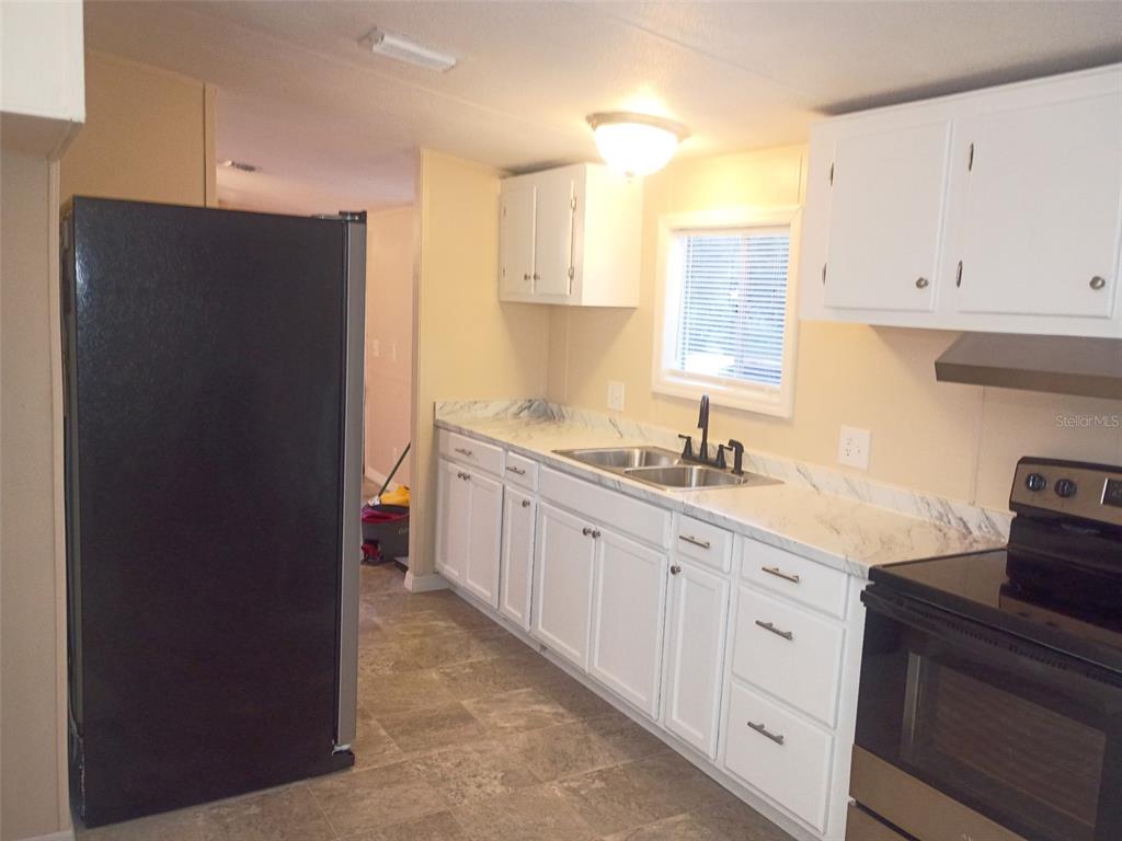 A kitchen features white cabinets, marble-look countertops, a black refrigerator, and a stainless steel stove — 6910 BROOKRIDGE TRAIL, LAKELAND, FL